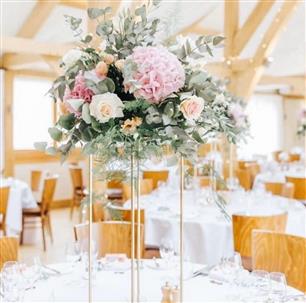 Bassmead Manor Barns, nestled in the picturesque countryside on the Bedfordshire/Cambridgeshire border, is a stunning modern barn wedding venue. Surrounded by tranquil landscapes and featuring a quaint stream and courtyard, Bassmead Manor Barns offers a secluded and romantic setting for couples to tie the knot. This couple had tall glad stands with a full floral arrangement on top in pastel pinks and peaches