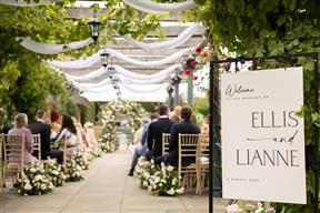 View from the back of the outdoor wedding ceremony with guests seated and flower meadow arrangements down the aisle