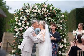 Shortmead House wedding flowers. Bedfordshire outdoor wedding venue ceremony with full flower arch and couple kissing in front of it