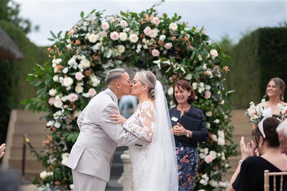 Shortmead House wedding flowers. Bedfordshire outdoor wedding venue ceremony with full flower arch and couple kissing in front of it