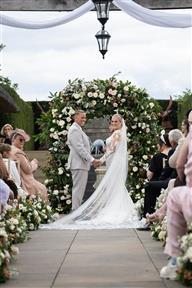 Outdoor wedding ceremony taking place with flower meadows down the aisle and a large floral arch